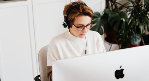 woman typing on laptop and listening through headphones