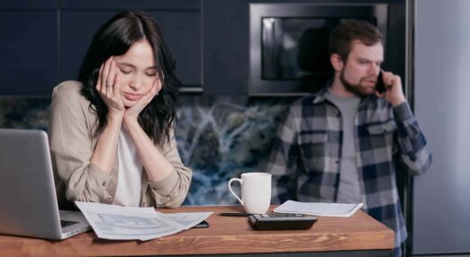 Woman with head in hands on computer and man on phone